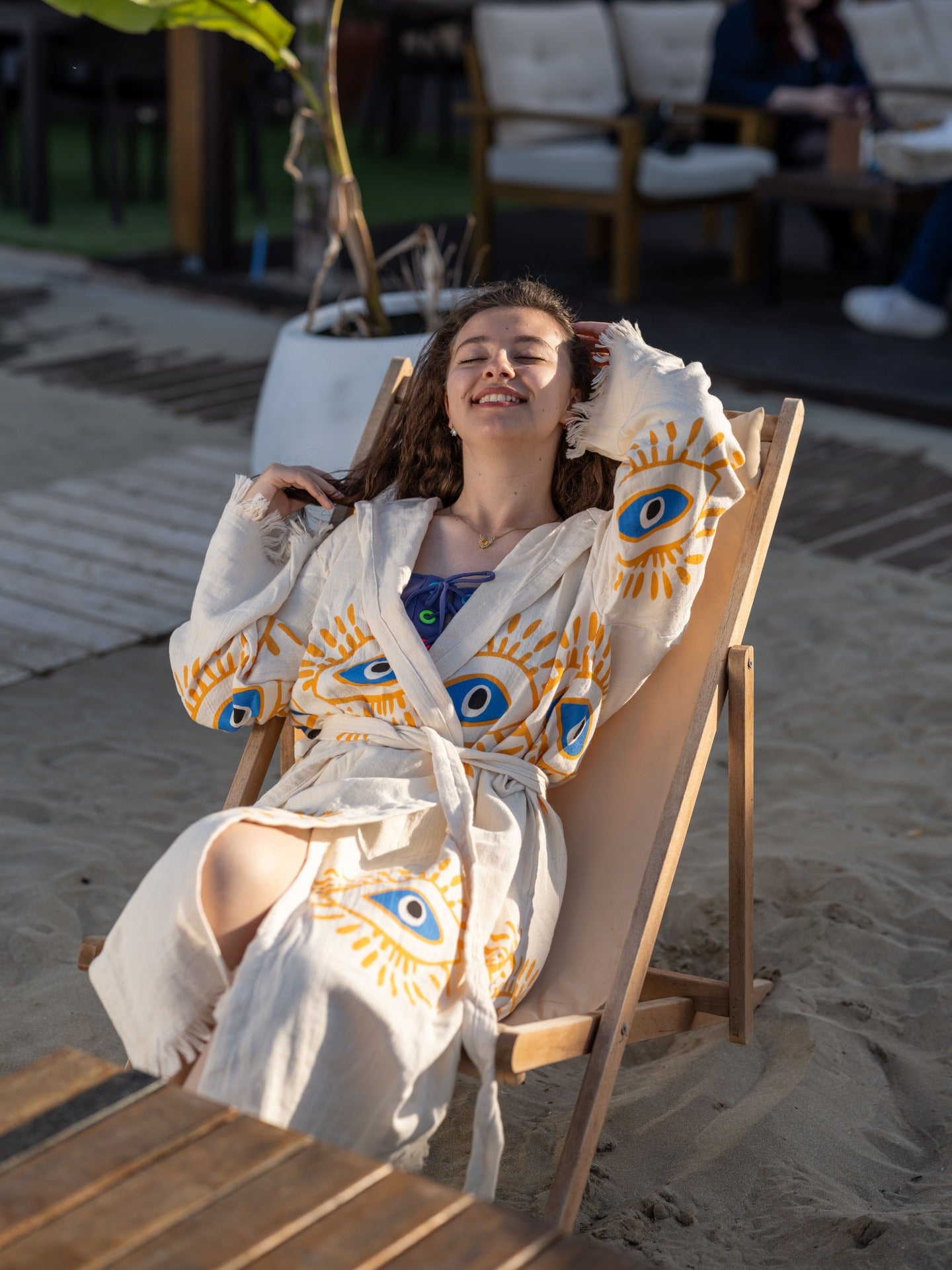 Woman in a robe with eye patterns sitting on a beach chair.