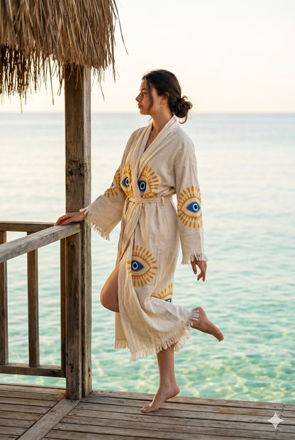 Woman in a robe with eye designs standing on a wooden deck by the water.