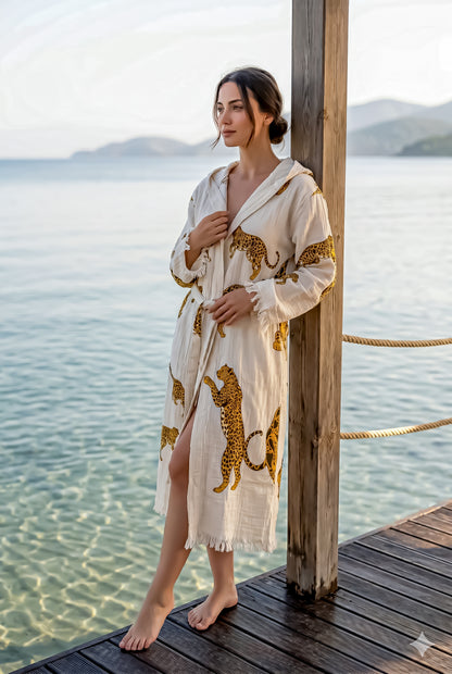 Woman in a leopard print robe standing on a wooden dock by a body of water.