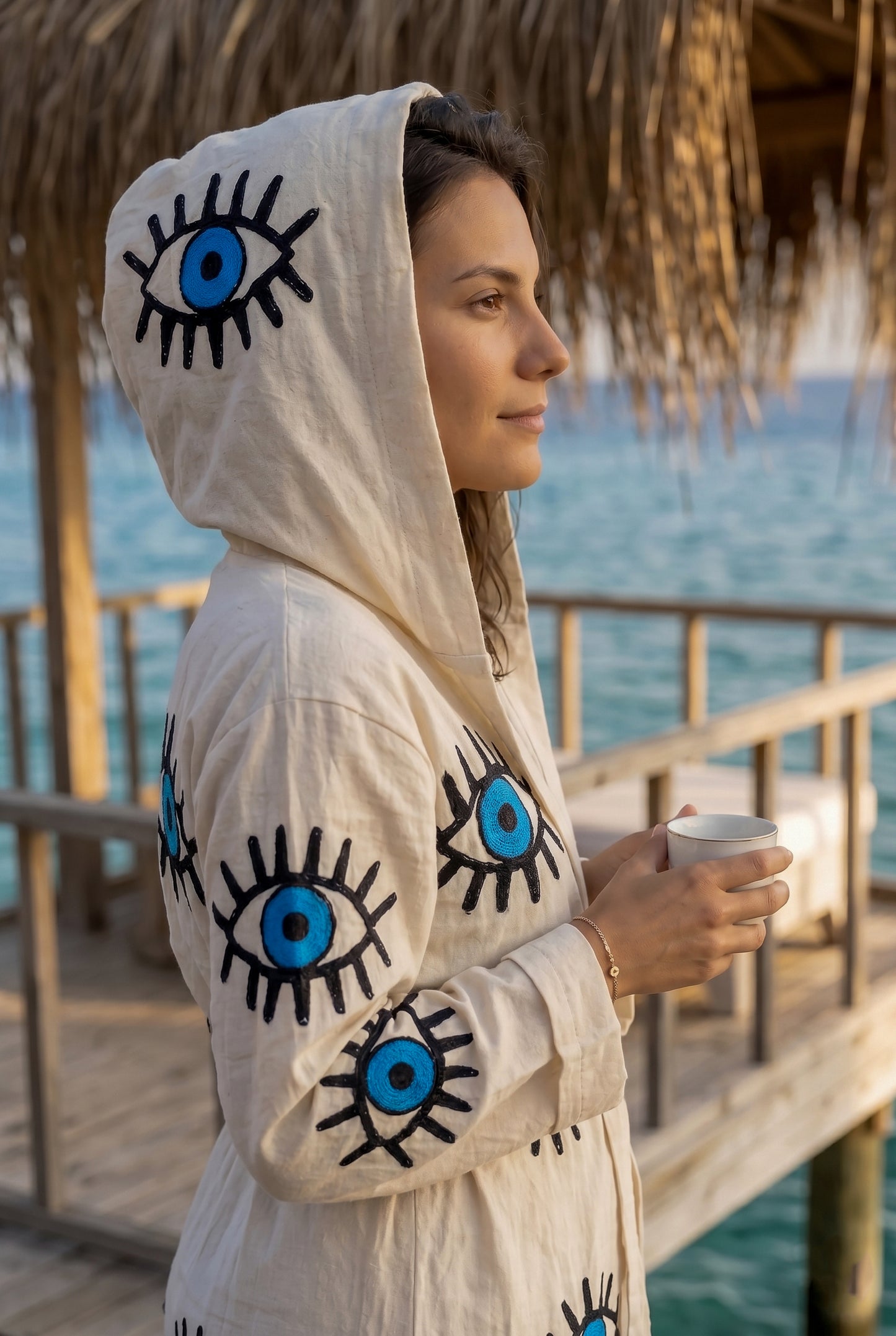 Woman wearing a hoodie with eye designs by the water