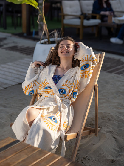 Woman in a robe with eye patterns sitting on a beach chair.